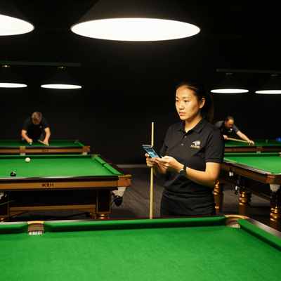 Snooker King floor manager checking a live table grid on her phone mid-floor